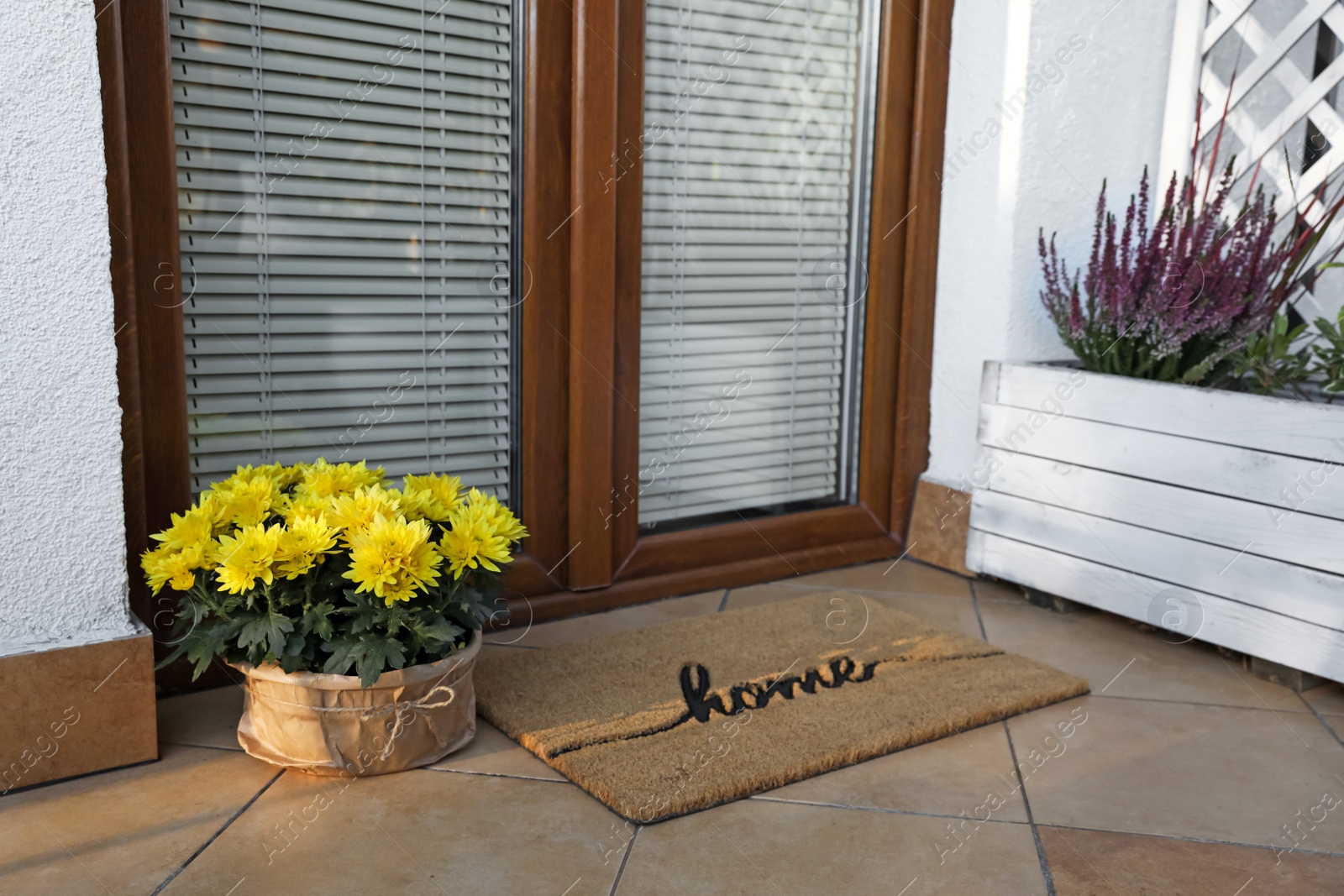 Photo of Doormat with word Home and flowers near entrance outdoors