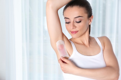 Woman doing armpit epilation procedure with wax strips indoors. Space for text