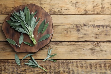 Board with fresh green sage on wooden table, flat lay. Space for text