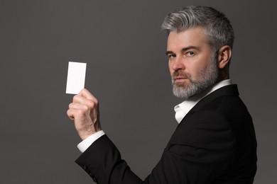 Handsome businessman holding blank business card on grey background