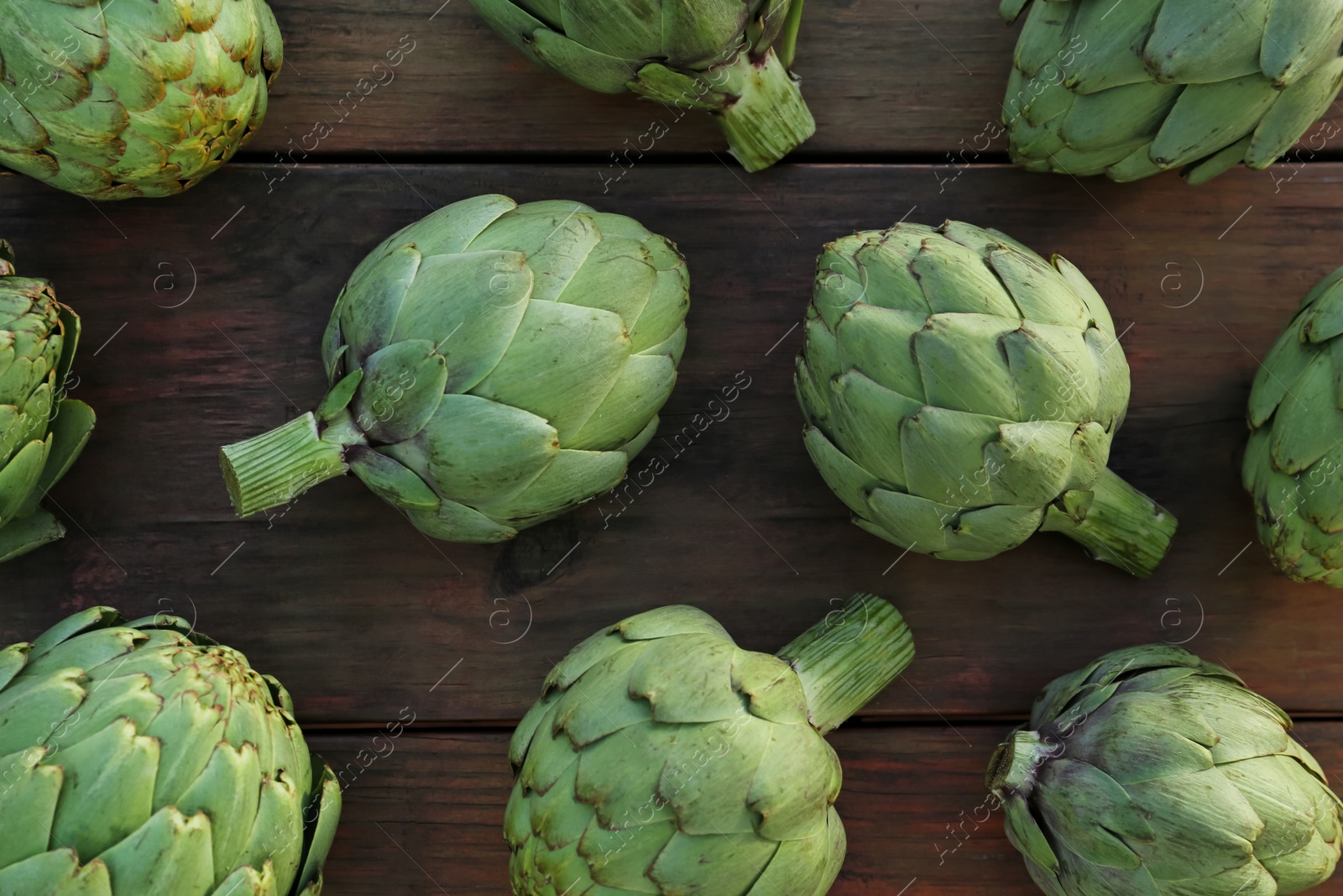 Photo of Whole fresh raw artichokes on wooden table, flat lay