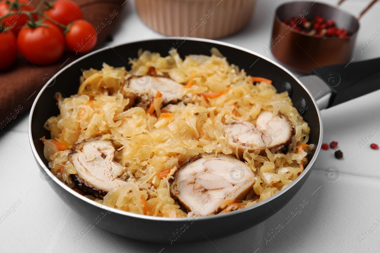 Photo of Frying pan with sauerkraut, and chicken on white tiled table