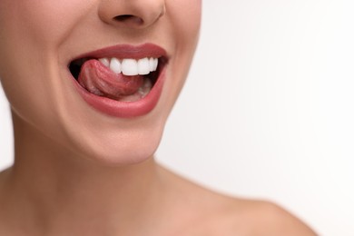 Woman with beautiful lips licking her teeth on white background, closeup. Space for text