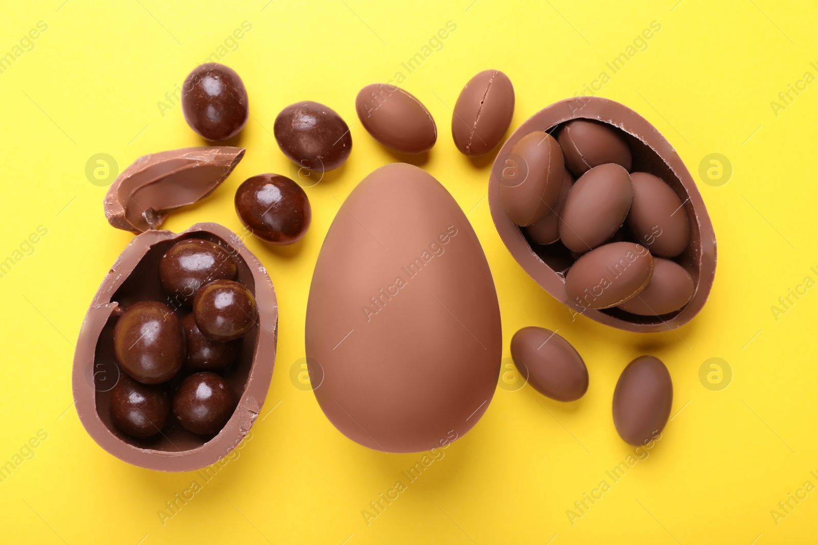 Photo of Delicious chocolate eggs and sweets on yellow background, flat lay