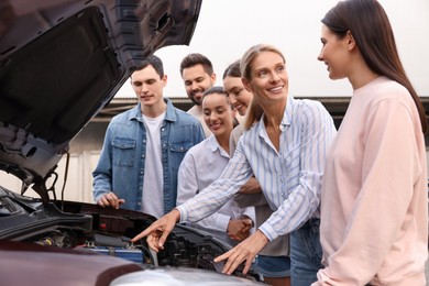 Photo of Driving school. Teacher explaining car engine to group outdoors