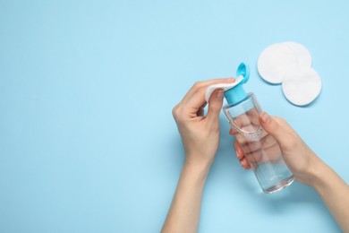 Photo of Woman pouring makeup remover onto cotton pad on light blue background, top view. Space for text