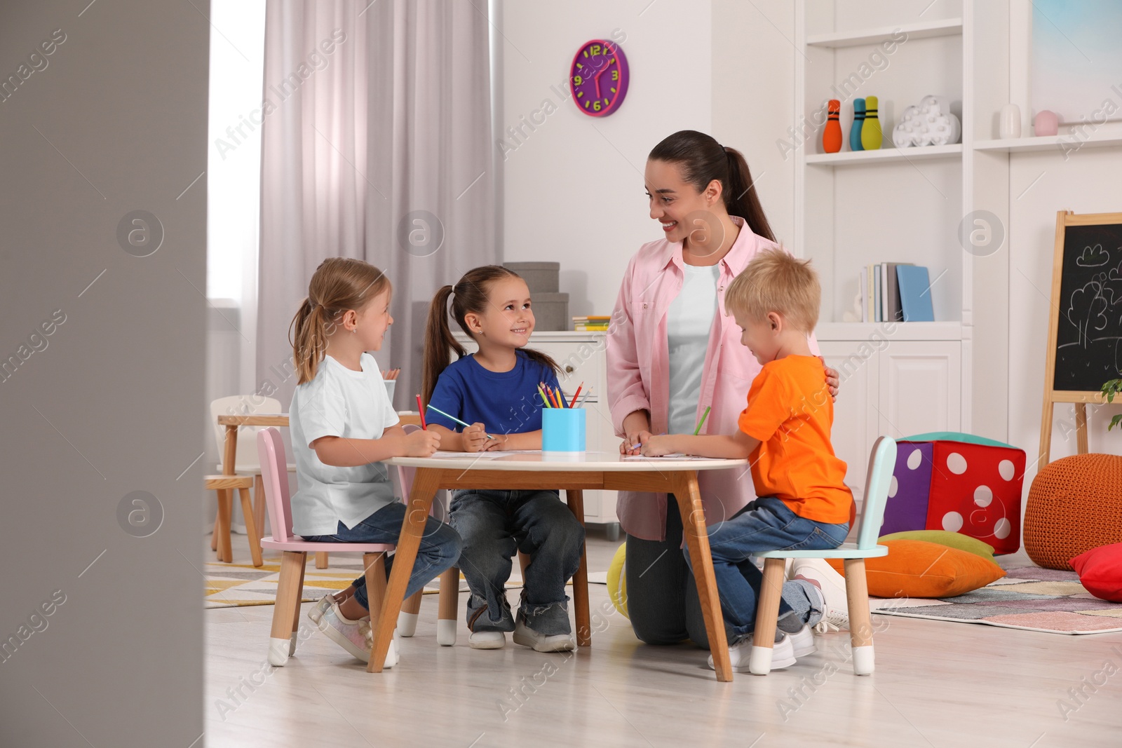 Photo of Nursery teacher and group of cute little children drawing at desk in kindergarten. Playtime activities