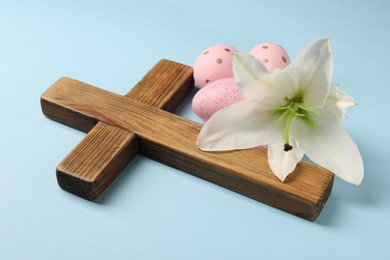 Photo of Wooden cross, painted Easter eggs and lily flower on light blue background, closeup