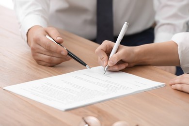 Photo of Businesspeople signing contract at wooden table, closeup