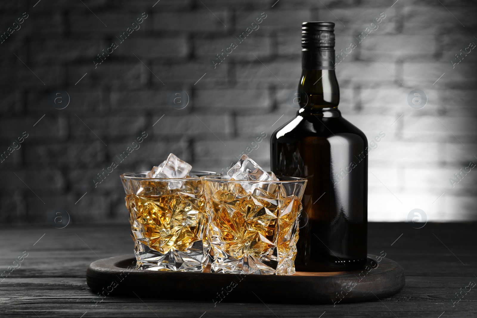 Photo of Whiskey with ice cubes in glasses and bottle on black wooden table