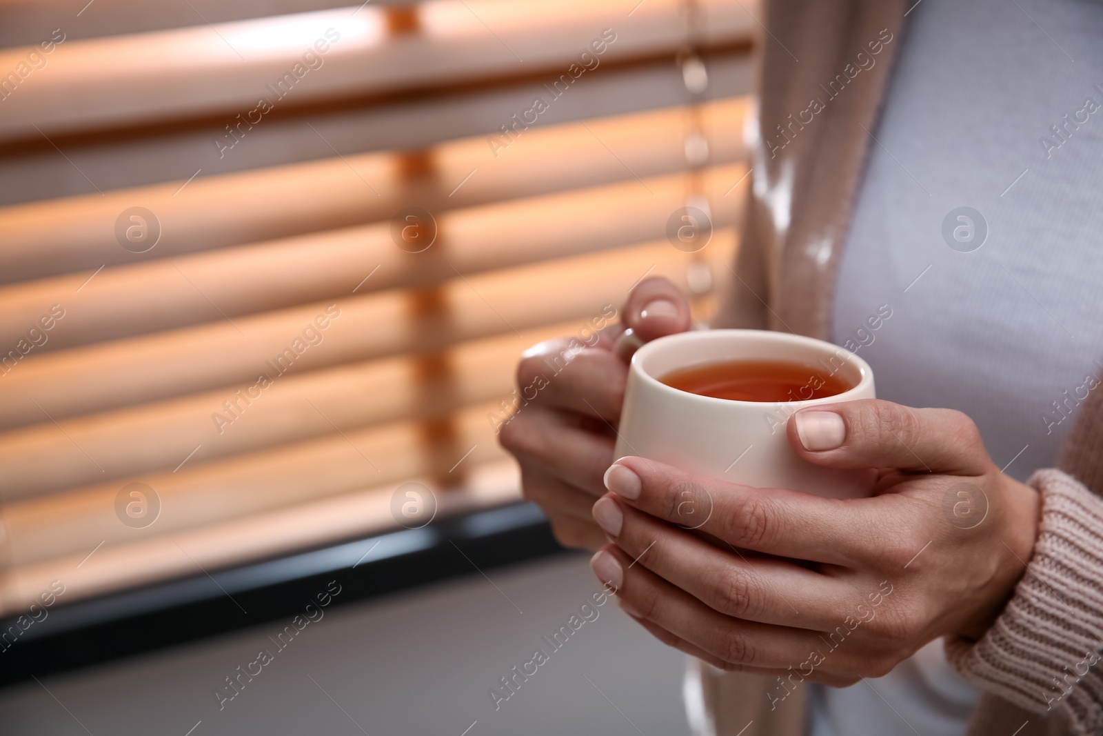 Photo of Woman with cup of hot tea indoors, closeup. Cozy home atmosphere