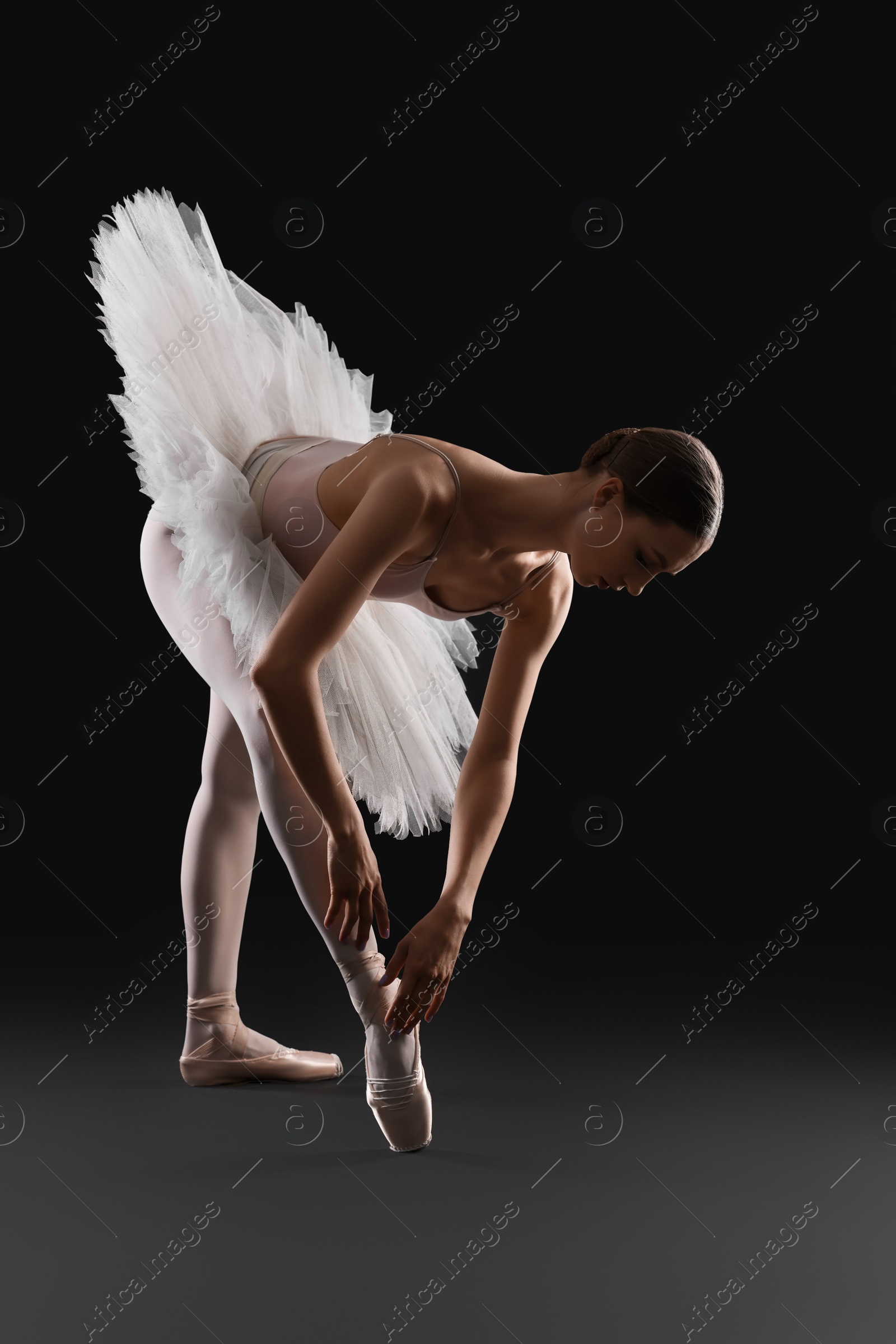 Photo of Young ballerina practicing dance moves on black background