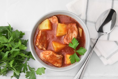 Photo of Delicious goulash in bowl on white tiled table, flat lay