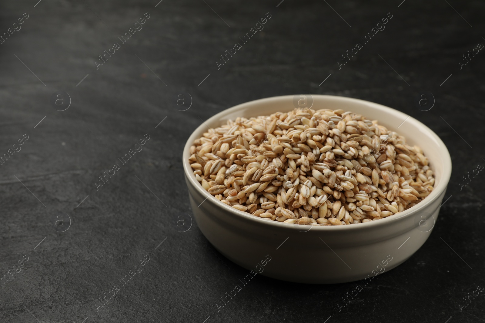 Photo of Dry pearl barley in bowl on dark gray table, space for text