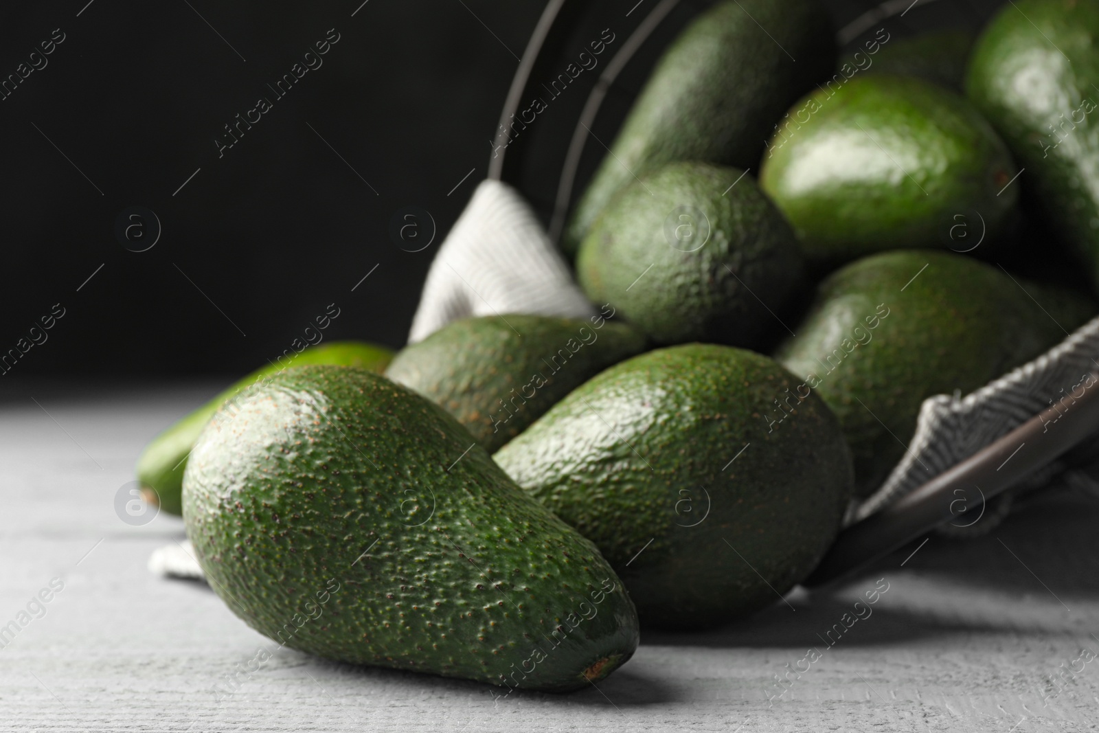 Photo of Delicious ripe avocados on grey wooden table against dark background