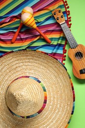Photo of Mexican sombrero hat, guitar, maracas and colorful poncho on green background, flat lay