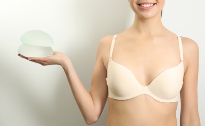 Woman holding silicone implants for breast augmentation on white background, closeup. Cosmetic surgery