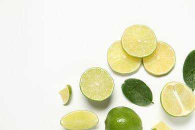 Photo of Whole and cut fresh ripe limes with green leaves on white background, flat lay