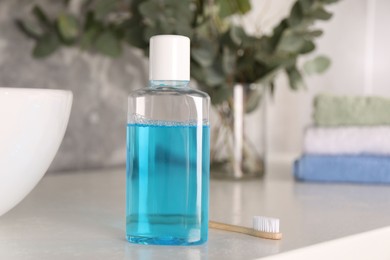 Photo of Bottle of mouthwash and toothbrush on white table in bathroom