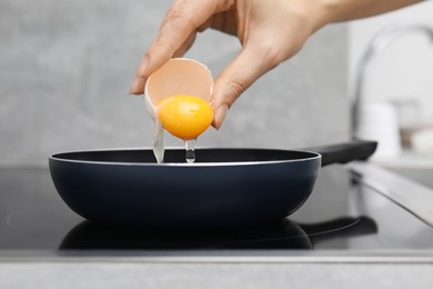 Photo of Woman adding raw egg into frying pan indoors, closeup