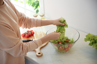 Photo of Young woman cooking salad at table in kitchen, closeup