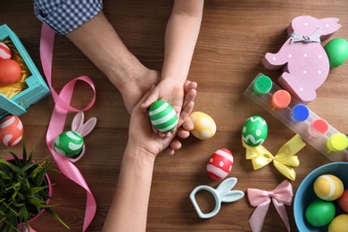 Photo of Father, mother and their child holding painted Easter egg on wooden background, top view