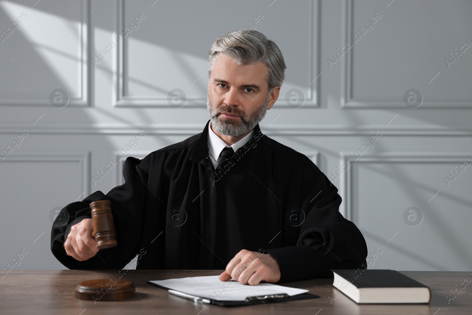 Photo of Judge with gavel, papers and book sitting at wooden table indoors