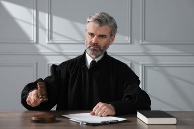 Judge with gavel, papers and book sitting at wooden table indoors