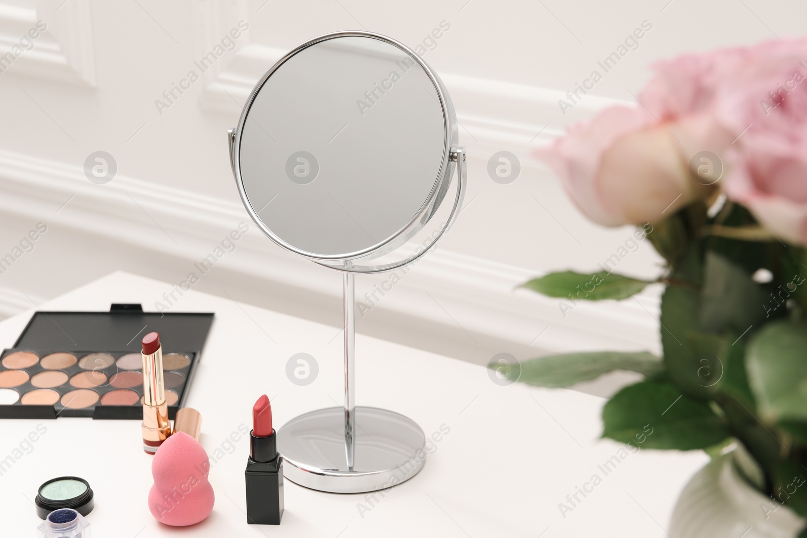 Photo of Mirror, cosmetic products and pink roses on white dressing table, closeup