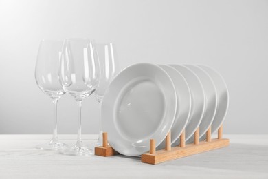 Photo of Set of clean plates and glasses on white wooden table against light background