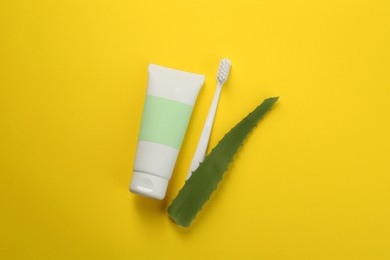 Aloe vera toothpaste in blank tube, brush and green leaf on yellow background, flat lay. Space for text