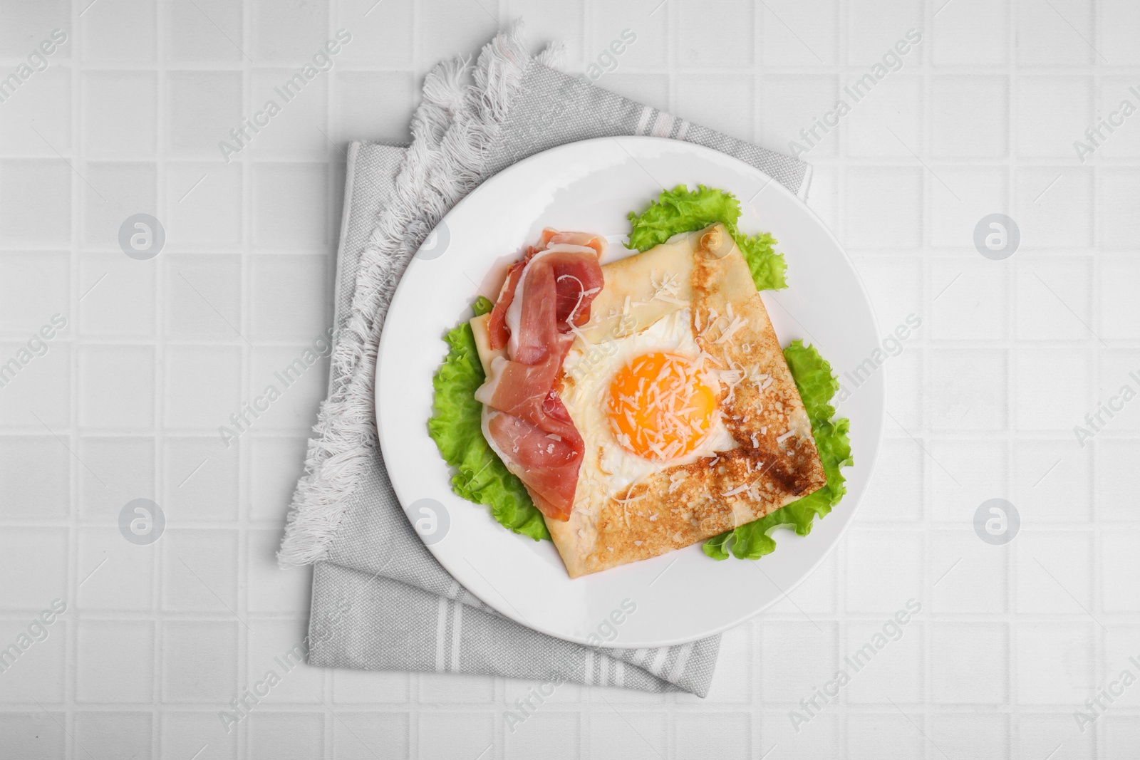 Photo of Delicious crepe with egg served on white tiled table, flat lay. Breton galette