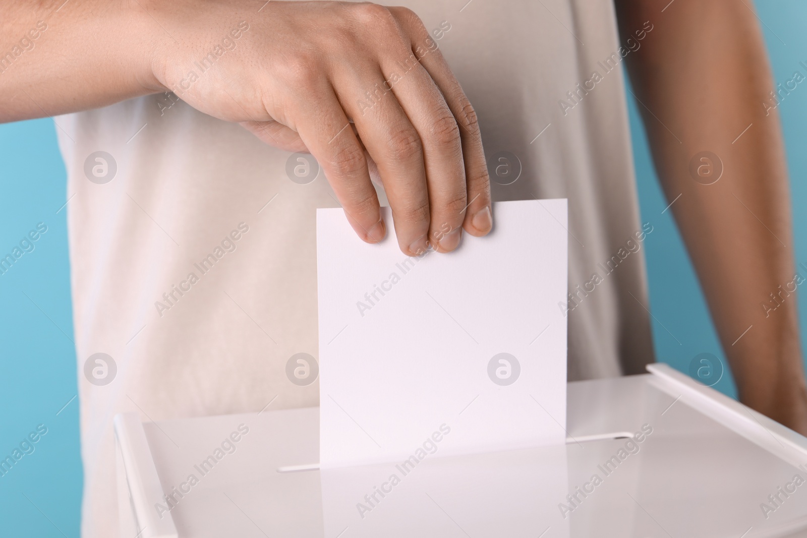 Photo of Man putting his vote into ballot box on light blue background, closeup