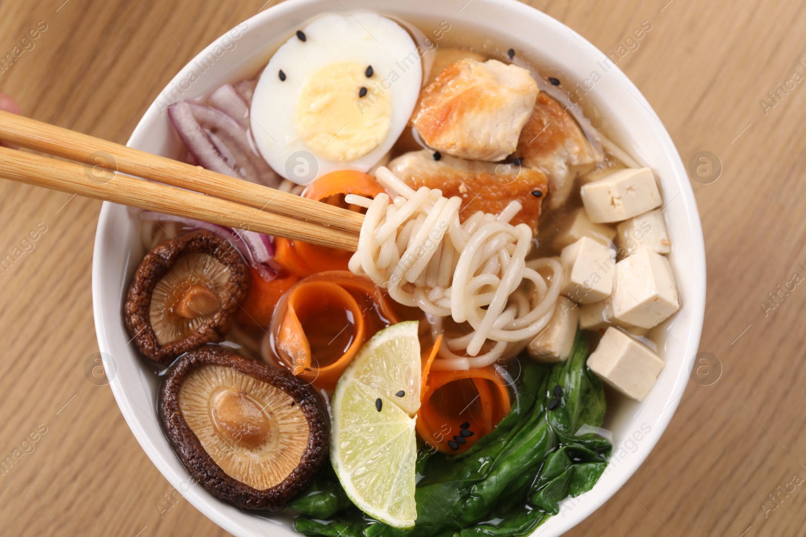 Photo of Eating delicious ramen with chopsticks at wooden table, top view. Noodle soup