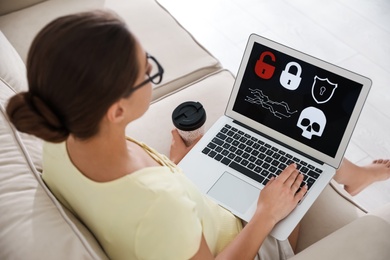 Woman holding laptop with virus illustration on screen at home