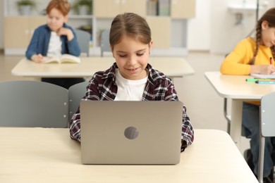 Photo of Smiling little girl with laptop studying in classroom at school
