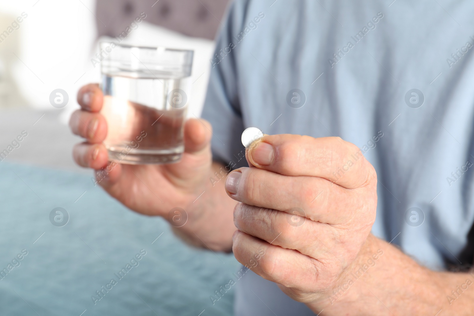 Photo of Senior man holding pill and glass of water indoors, closeup