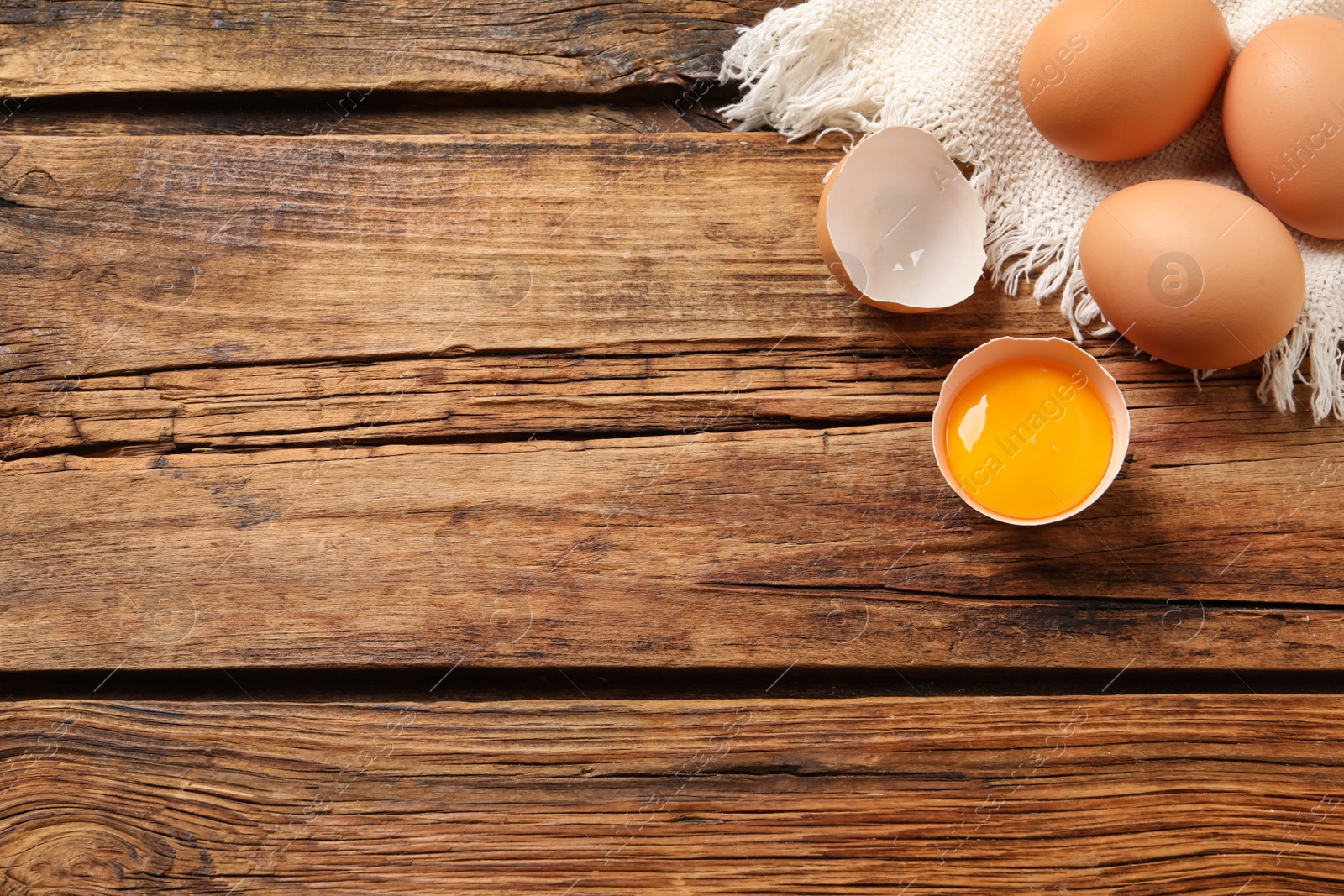 Photo of Raw chicken eggs and shell with yolk on wooden table, flat lay. Space for text