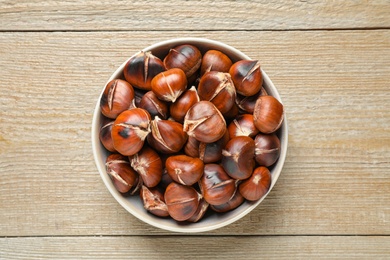 Photo of Delicious roasted edible chestnuts on wooden table, top view