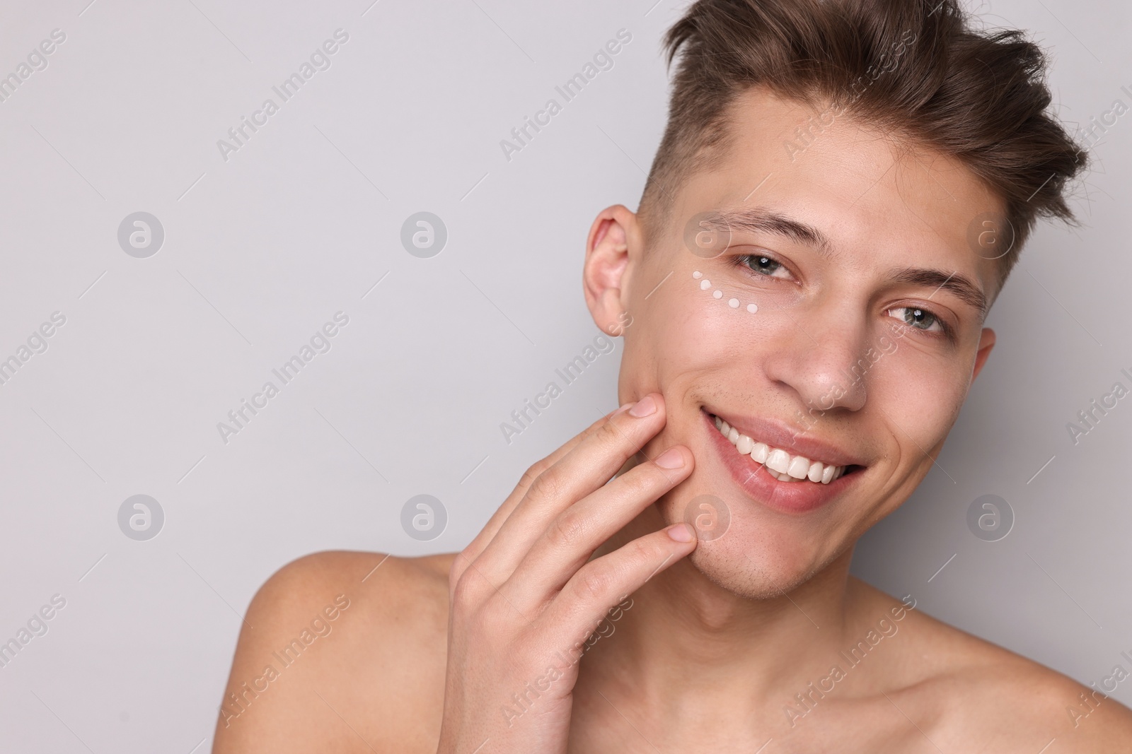 Photo of Handsome man with moisturizing cream on his face against light grey background. Space for text