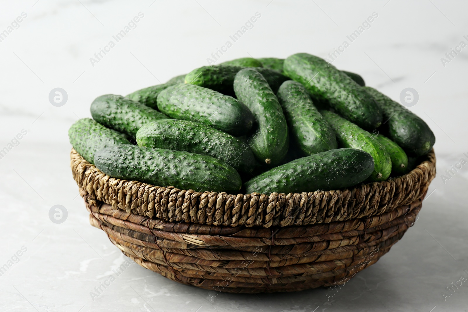 Photo of Fresh ripe cucumbers in wicker basket on marble table