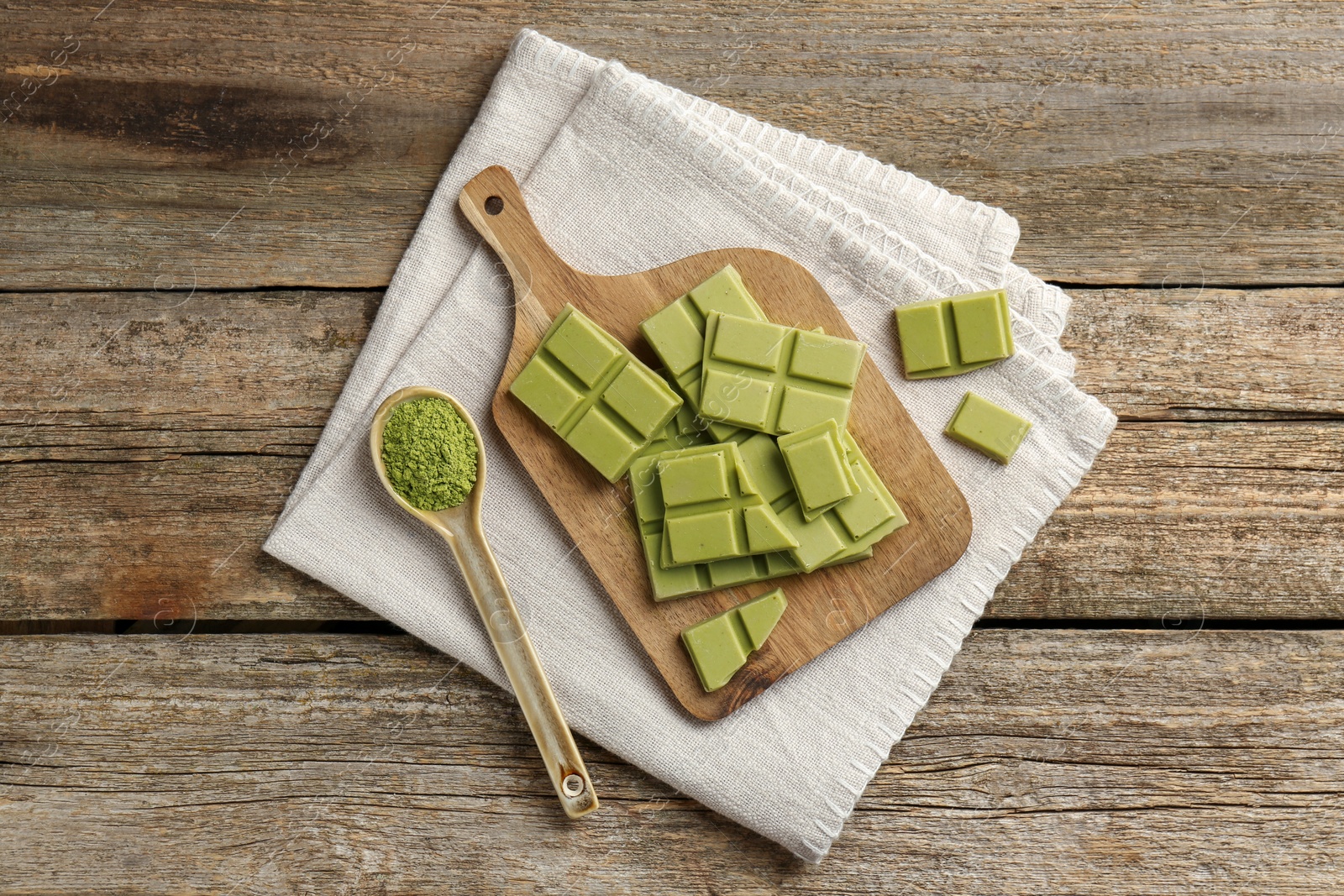 Photo of Pieces of tasty matcha chocolate bar and powder in spoon on wooden table, top view