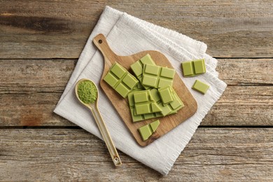 Pieces of tasty matcha chocolate bar and powder in spoon on wooden table, top view