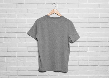 Photo of Hanger with blank t-shirt on white brick wall. Mock up for design