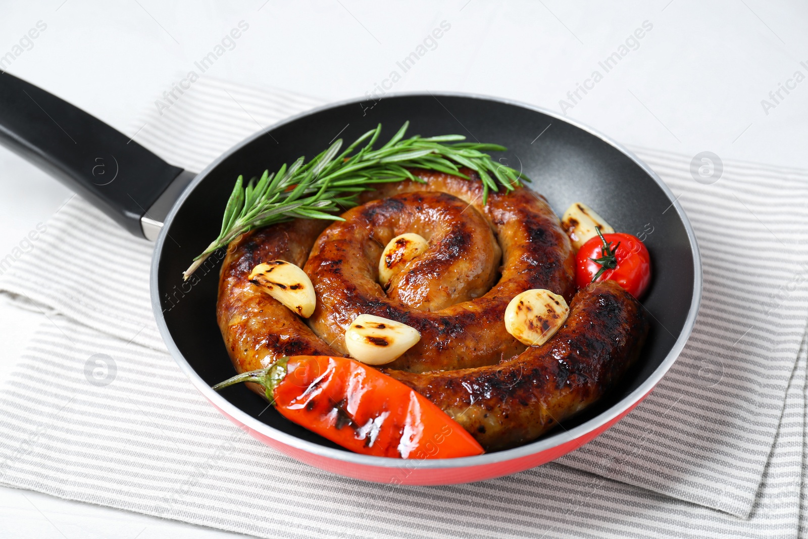 Photo of Delicious homemade sausage with garlic, tomato, rosemary and chili in frying pan on table, closeup