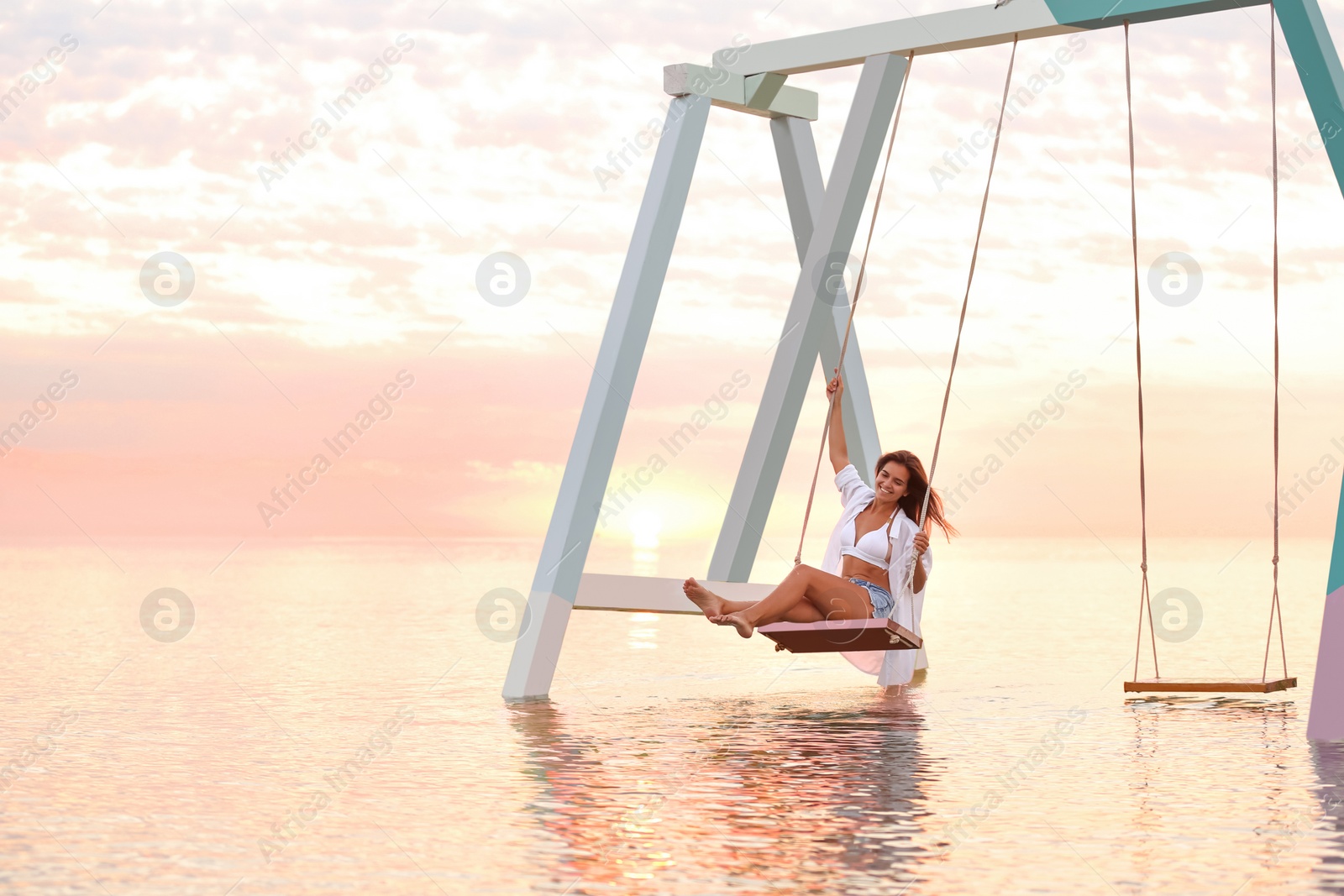 Photo of Young woman enjoying sunrise on swing over water