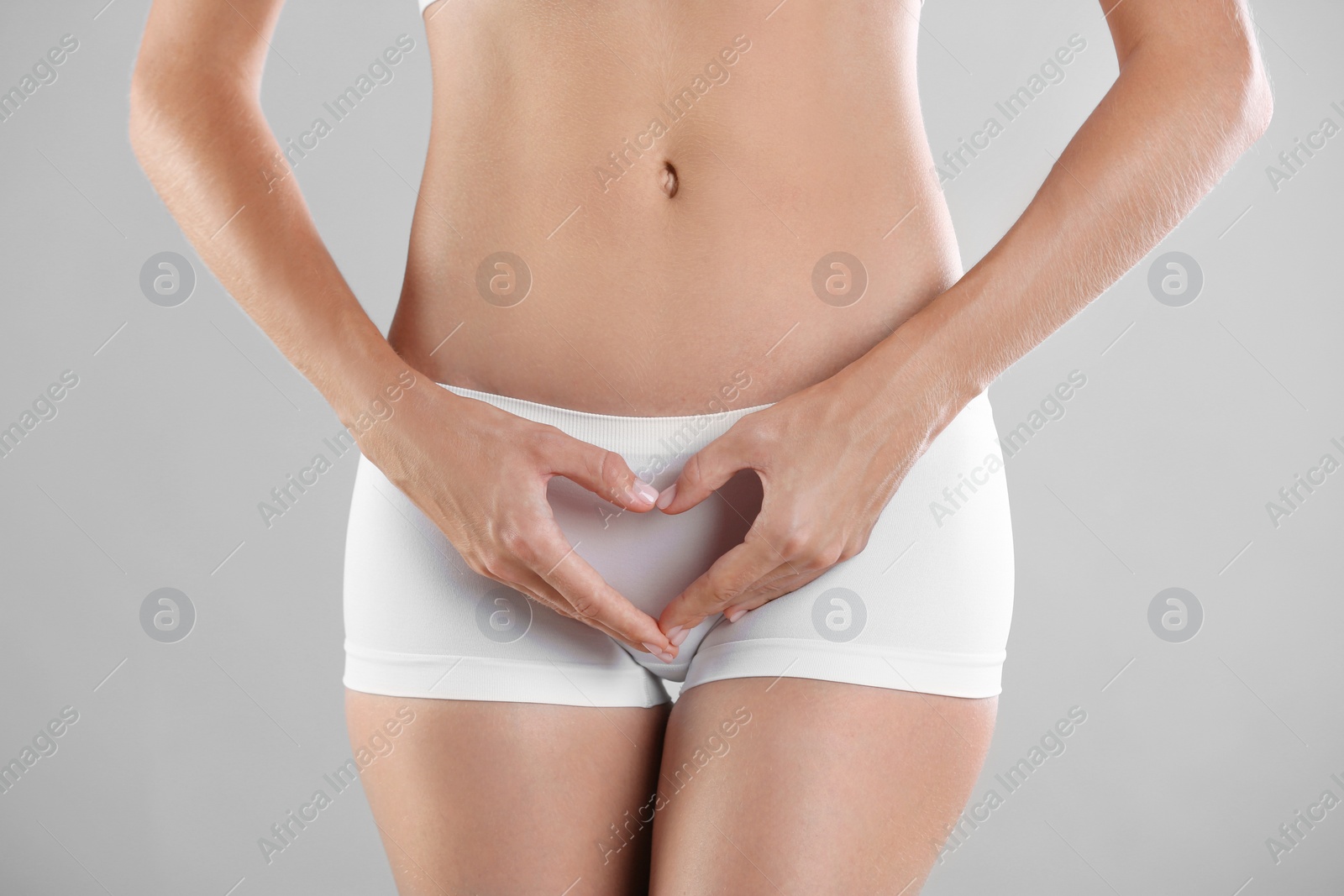 Photo of Young woman holding hands in heart shape on grey background. Gynecology concept