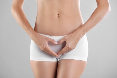 Young woman holding hands in heart shape on grey background. Gynecology concept