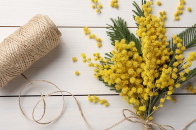 Beautiful mimosa flowers and twine on white wooden table, flat lay