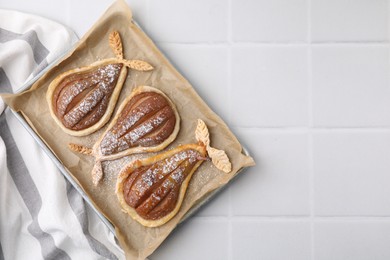 Delicious pears baked in puff pastry with powdered sugar on white tiled table, top view. Space for text